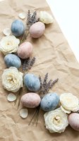 Easter eggs in pastel blue and pink with white roses and lavender sprigs arranged on kraft paper background for spring holiday celebration decor.