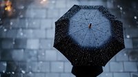 Silhouette of person holding umbrella in heavy rain against moody urban background, raindrops creating atmospheric bokeh effect in dark blue tones.