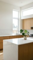 Bright modern kitchen featuring white quartz countertops, natural wood cabinetry, stainless steel appliances, and large windows flooding the space with natural light. Potted plant adds greenery.