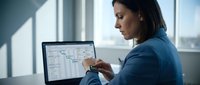Professional businesswoman analyzing financial data on laptop computer in modern office environment with natural lighting from windows.