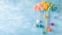 Colorful yarn balls arranged as clouds with hanging drops against blue sky background, creating whimsical craft composition for nursery decor and DIY projects.