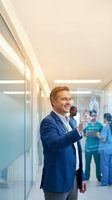 Middle-aged Caucasian businessman in navy suit interacting with holographic medical interface displaying heart anatomy in modern hospital corridor.