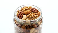 Mixed nuts in glass jar with walnuts, almonds, pecans and cashews for healthy snacking and cooking ingredients on white background.