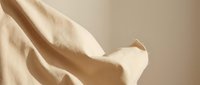 Soft beige fabric with elegant draping and gentle folds creating luxurious textile waves against neutral background for fashion and interior design projects.