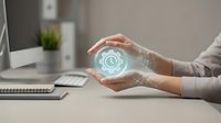 Hands holding glowing digital clock icon with holographic light effect at office desk workspace for time management and scheduling concepts.