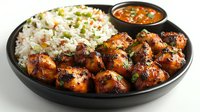 Grilled spicy chicken pieces served with fragrant rice and red chili sauce in black plate, garnished with fresh herbs and vegetables for restaurant menu.
