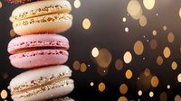 Delicate French macarons stacked in white, pink and gold colors against dark background with magical bokeh lights creating festive atmosphere.