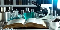 Laboratory workspace with open scientific book, microscope, turquoise liquid in glass flasks, test tubes and research equipment on dark background. Scientific research concept.