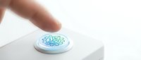 Finger pressing white circular button with green brain circuit pattern on clean surface for technology interface activation.