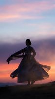 Silhouette of woman dancing in flowing dress against dramatic sunset sky with pink and orange clouds creating romantic atmospheric scene.