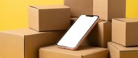 Modern smartphone with blank white screen resting on stack of brown cardboard shipping boxes against vibrant yellow background for e-commerce delivery.