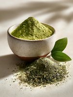 Fine matcha green tea powder in ceramic bowl with dried tea leaves on neutral background, highlighting Japanese tea ceremony tradition.