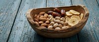 Wooden bowl filled with mixed nuts, dates and dried fruits on rustic blue wooden table. Healthy snacking, organic food ingredients for cooking and baking.