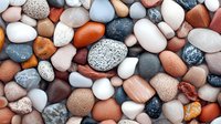 Colorful smooth river rocks and pebbles in various sizes creating natural texture pattern. Mixed stone collection with earth tones for spa and wellness designs.