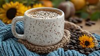 Speckled ceramic mug filled with hot chocolate on knitted coaster, surrounded by coffee beans and bright sunflowers, creating cozy autumn atmosphere.