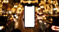 Hand holding smartphone with blank white screen against blurred golden bokeh lights background at night for mobile app mockup and digital display.