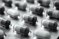 Close up macro shot of pharmaceutical capsules and pills in blister pack, showing transparent and solid medication in black and white tones. Medical concept.