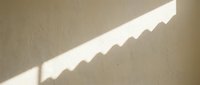 Sunlight streaming through venetian blinds creates geometric shadow patterns on neutral beige wall surface, suitable for backgrounds and design projects.
