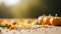 Autumn harvest scene with orange pumpkins, colorful fall leaves, and scattered seeds on wooden surface with warm golden sunlight creating cozy seasonal atmosphere.