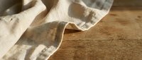 Soft beige linen fabric with natural texture draped elegantly on rustic wooden surface creating warm minimalist composition for home decor and textile design.