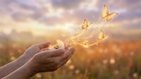 Hands releasing glowing butterflies at sunset symbolizing freedom, hope and transformation in nature with warm golden light and dreamy sky background.