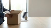 Professional businessman in suit carrying cardboard box in modern office during relocation or job transition with natural window lighting.