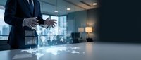Businessman in formal suit manipulating holographic world map and global network connections on conference table, representing international business, digital transformation, and global commerce.