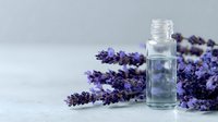 Glass essential oil bottle with fresh lavender sprigs on light gray background, perfect for aromatherapy and wellness product marketing.