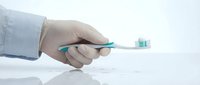 Close-up of hand in medical glove holding toothbrush with turquoise bristles on white background, dental hygiene and oral care concept for healthcare design.
