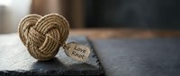 Handmade rope heart with love knot message tag on rustic wooden surface for romantic Valentine's Day greeting cards and wedding decorations.