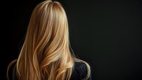 Blonde wavy hair flowing against dark background showcases natural highlights and healthy shine, demonstrating professional hair care and styling techniques.