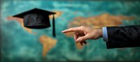 Business hand pointing at graduation cap floating over blurred world map background, symbolizing global education and academic achievement opportunities.