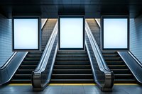 Modern subway station interior with parallel escalators and stairs leading upward, illuminated by bright light panels creating symmetrical architectural composition.