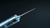 Medical syringe with needle on dark background, dramatic lighting creates mysterious atmosphere. Healthcare and vaccination concept for medical presentations.