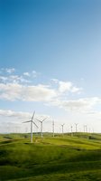 Wind turbines scattered across rolling green hills under a bright blue sky with white clouds, representing renewable energy and sustainable power generation for environmental and industrial applications.