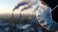 Person wearing protective face mask with industrial smokestacks emitting pollution in blurred background during sunset, environmental health concept.
