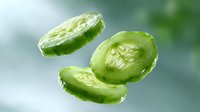 Fresh cucumber slices floating in air against blurred green background, showing juicy texture and translucent inner pattern of seeds and flesh.