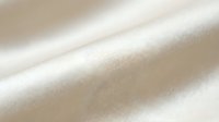 Soft beige fabric texture with gentle folds and natural lighting creating elegant waves and shadows for luxury textile and fashion design projects.