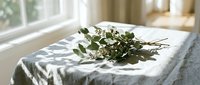 Fresh eucalyptus branches arranged on white linen fabric by sunny window creating natural spa atmosphere for wellness and aromatherapy concepts.