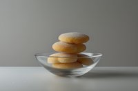 Stacked sugar-coated cookies in clear glass bowl against neutral background, minimalist food composition with soft natural lighting and gentle shadows.