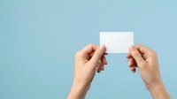 Close-up of hands holding blank white card against light blue background, suitable for business cards, gift cards, or promotional material presentations.
