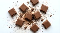 Chocolate squares and cocoa powder scattered on white surface, ideal for confectionery, baking, and food styling projects.