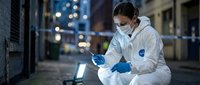 Forensic scientist in protective suit analyzing evidence with laptop computer at urban crime scene during nighttime investigation.