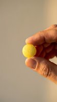 Close-up of hand holding small yellow sphere against neutral background, suitable for healthcare, pharmaceutical, supplement, or product showcase concepts.