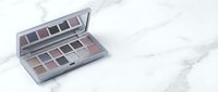 Open eyeshadow palette with neutral brown and pink tones on white marble surface for beauty and makeup applications.