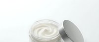 Creamy white moisturizer or skincare product in open glass jar with gray lid on white background, isolated for cosmetics packaging and beauty product design.