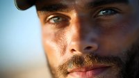 Close up portrait of young African American man with beard and intense blue eyes in warm sunset lighting, dramatic shadows highlighting facial features.