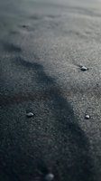 Close-up of dark volcanic sand beach with small pebbles and natural texture, shallow depth of field creating atmospheric coastal background.