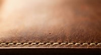 Brown leather surface with detailed stitching showcasing craftsmanship and texture for luxury goods, fashion accessories, and artisan products.