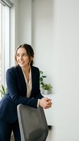 Young professional businesswoman in navy suit sitting in modern office space looking optimistic and confident during corporate meeting or interview.